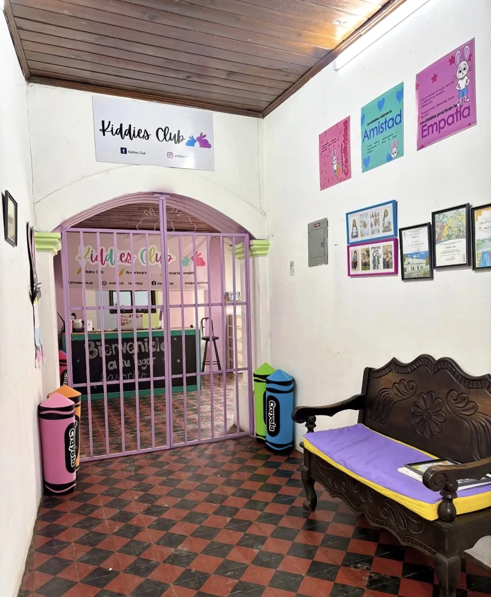 Entrada de Kiddies Club con su letrero, la reja lila y crayones gigantes de colores