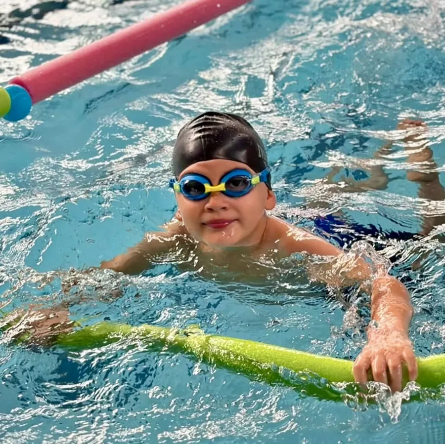 Niño con gorro y goggles nadando con un flotador en la piscina