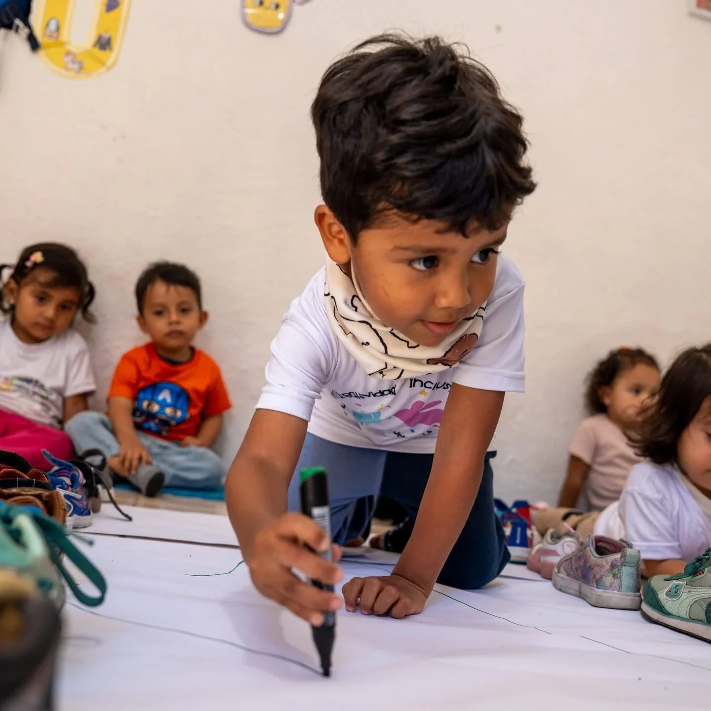 Niño de Kiddies Club dibujando con marcador en un papel grande en el suelo, con sus compañeros alrededor